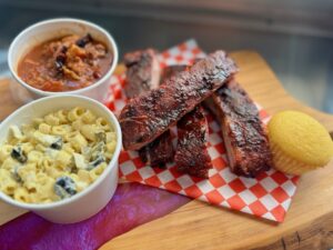 BBQ ribs with cornbread, pasta salad, beans, on a cutting board