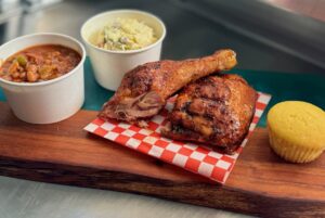 BBQ chicken with beans, corn bread, and potato salad on a cutting board