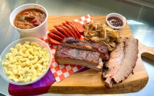 Various BBQ on a cutting board with bbq sauce and mac & cheese